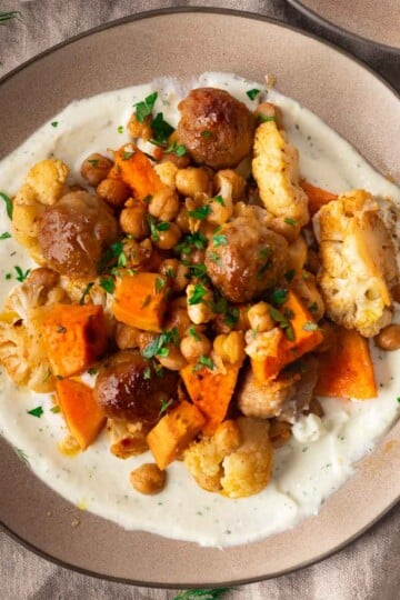 Sheet pan meatballs and veggies on a creamy sauce, garnished with herbs on a plate.