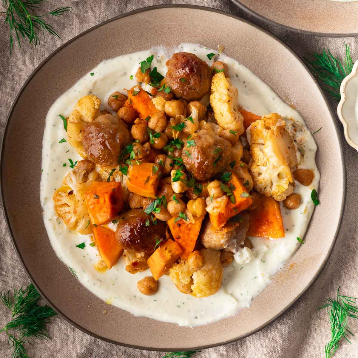 Sheet pan meatballs and veggies on a creamy sauce, garnished with herbs on a plate.