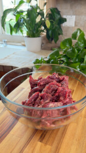 Bowl of raw beef strips on wooden countertop.