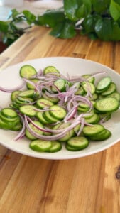 Sliced cucumbers and red onions in a white bowl.