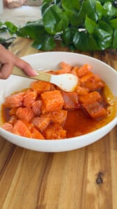 Diced salmon in sauce being stirred with a spoon in a white bowl.