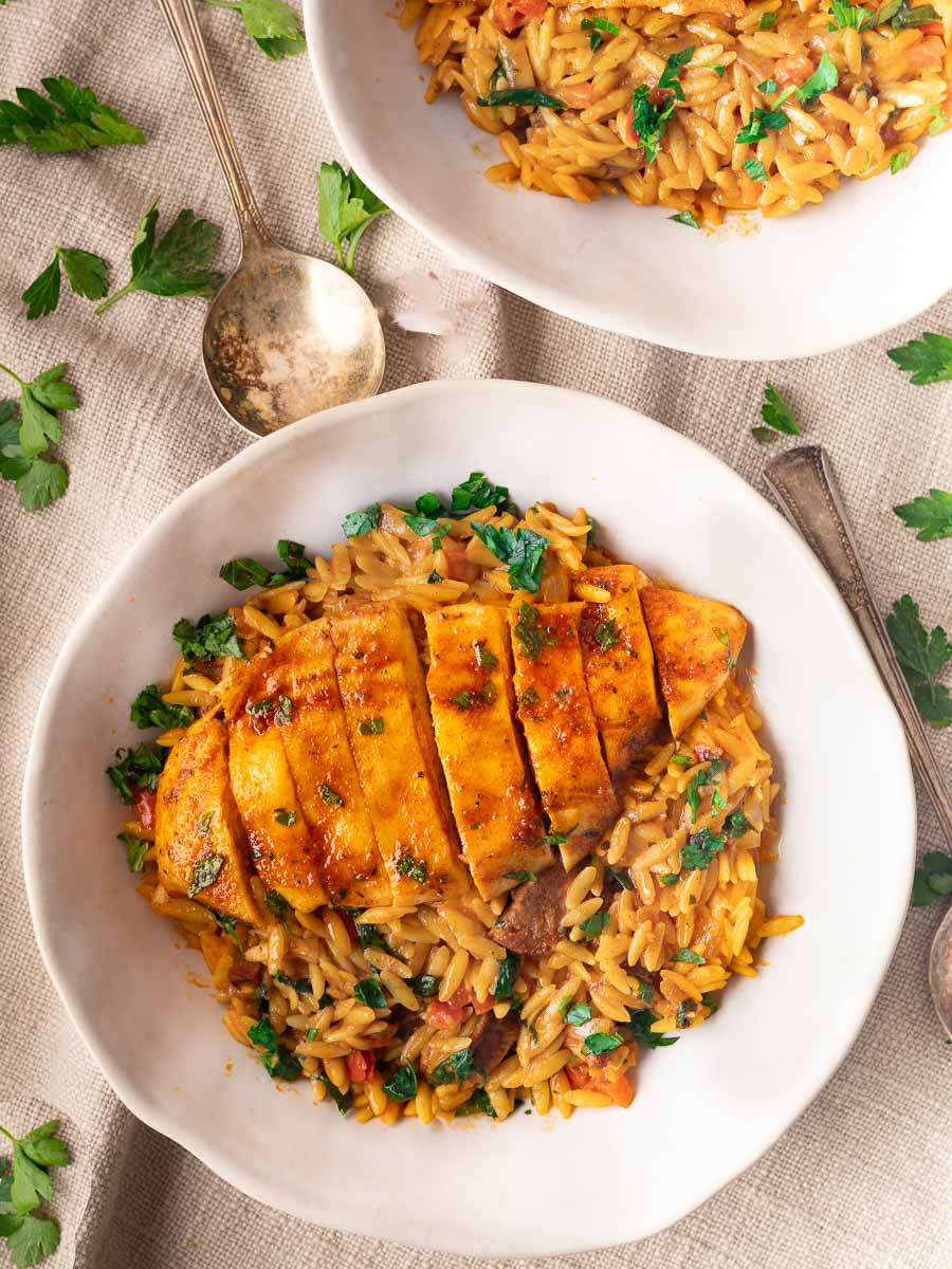 Chicken and chorizo orzo with herbs in a white bowl, garnished with parsley, spoon on the side.