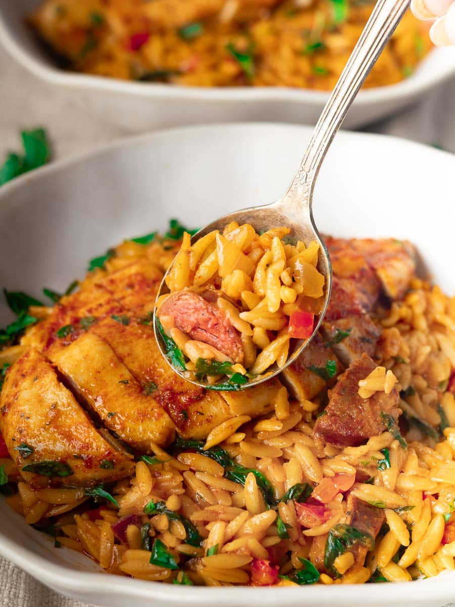 Spoonful of chicken-and-chorizo orzo with vegetables in a white bowl, garnished with herbs.