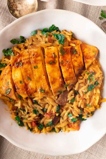 Chicken and chorizo orzo with herbs in a white bowl on a textured tablecloth.