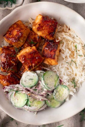 Honey harissa salmon with dill rice and cucumber salad on a white plate.