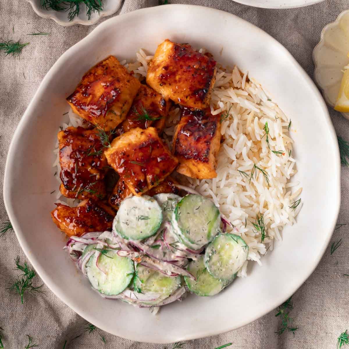 Honey harissa salmon with dill rice and cucumber salad on a white plate.