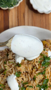 Spoon of yogurt over rice pilaf with herbs and ground meat on a wooden table.
