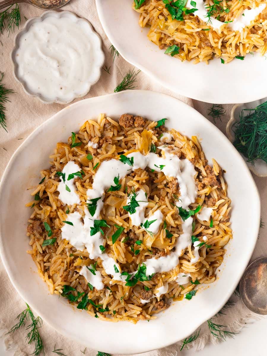 Stuffed cabbage bowl with ground meat and cabbage, topped with yogurt sauce and garnished with parsley on a white plate.