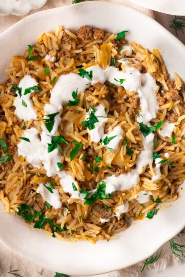 Stuffed cabbage bowl with ground meat, yogurt topping, and fresh parsley garnish in a white bowl.