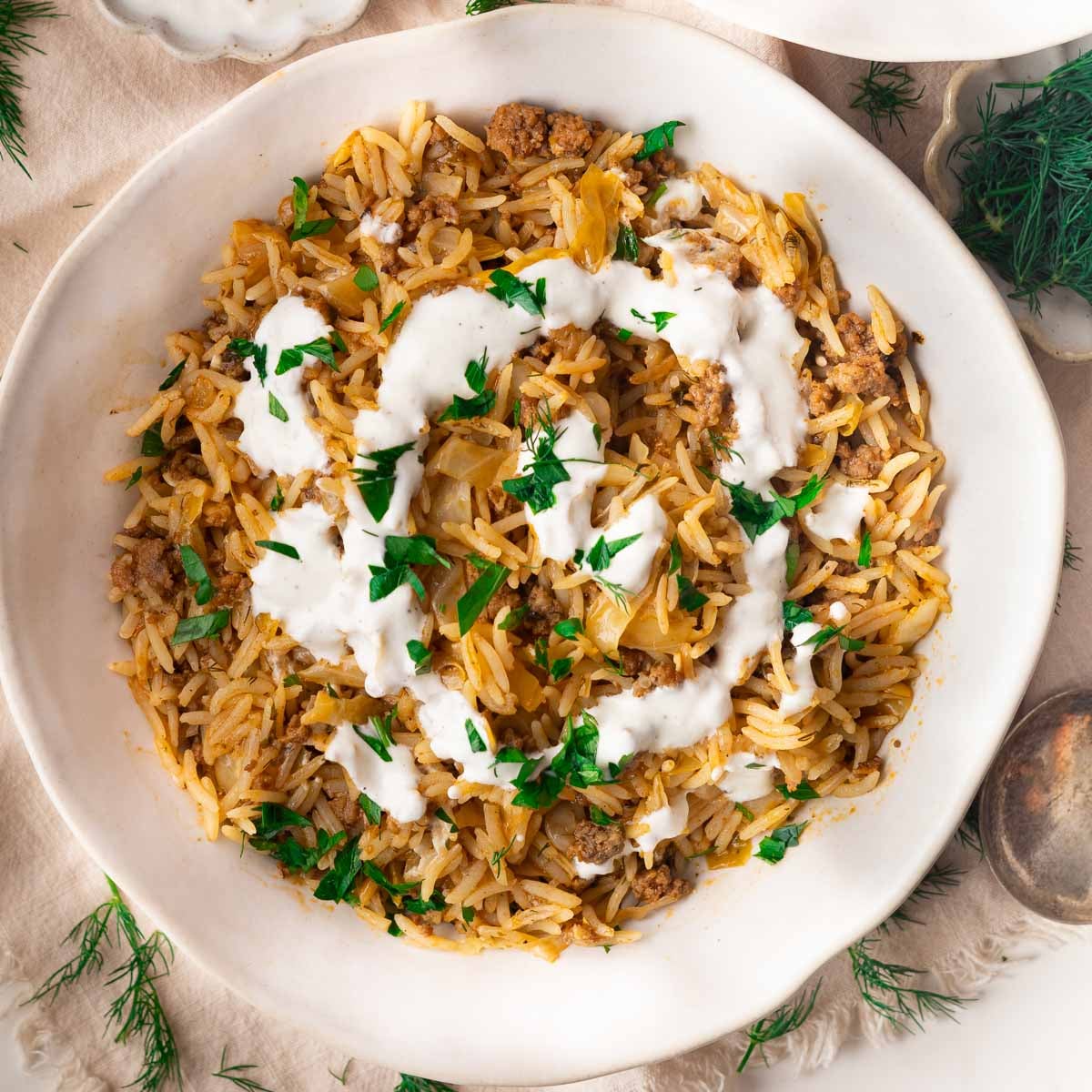 Stuffed cabbage bowl with ground meat, yogurt topping, and fresh parsley garnish in a white bowl.