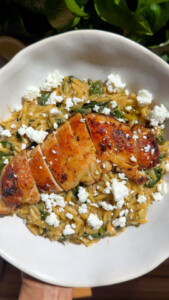 Grilled chicken on orzo with spinach and feta cheese in a white bowl.