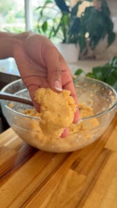 Close-up of hand holding dough ball over mixing bowl in a kitchen setting.