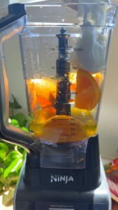 Blender with sliced oranges and liquid inside a clear container, set on a kitchen counter.