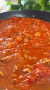 Hearty tomato meat sauce simmering in a black pan.