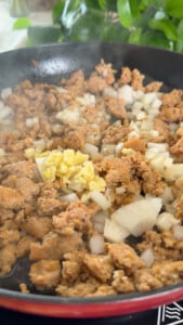 Cooking suasage with chopped onions and minced garlic in a skillet.