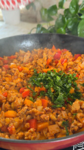 Sizzling skillet with ground meat, bell peppers, and fresh herbs cooking.