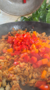 Chopped red and orange peppers added to sautéed ground meat in skillet.