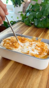Ice cream with flaky topping in white dish on wooden table.