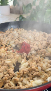 Cooking ground meat, onions, and tomato paste in a pan with steam rising.