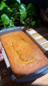 Golden loaf of cake in a loaf pan on a wooden table.
