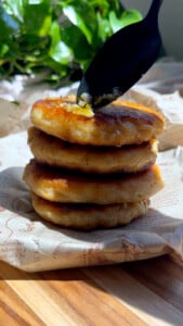 Tuna potato cakes with butter being spread by a spoon.