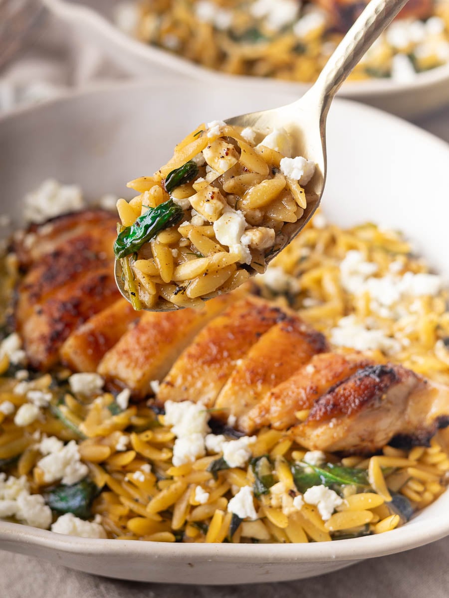 Chicken spinach orzo with feta, spinach, and sliced roasted chicken on a plate, close-up of a spoonful.