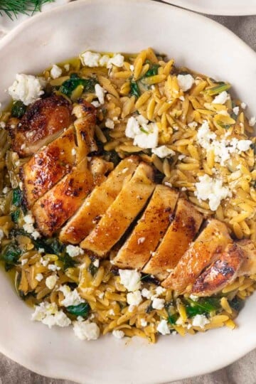Chicken spinach orzo with feta cheese garnish in a white bowl.