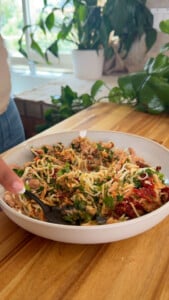 Mixing tuna with vegetables and herbs in a white bowl on a wooden countertop.