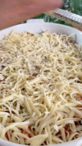 Grated cheese being sprinkled over a dish with a grater.