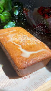Loaf cake with glaze and powdered sugar on parchment.