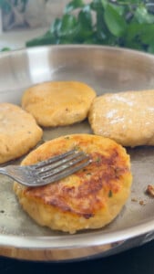 Pan-fried potato cakes with fork, golden brown and crispy crust in a skillet.