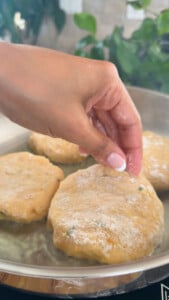Hand placing dough patties in a pan for frying.