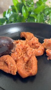 Raw sausage meat being cooked in a black frying pan with a wooden spoon.