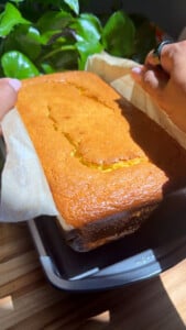 Freshly baked golden loaf cake being lifted from a baking pan with parchment paper.