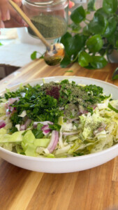 Fresh salad in a bowl with cabbage, onion, and herbs being seasoned.