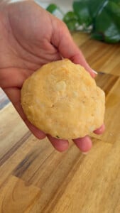 Hand holding a freshly-made tuna cake on a wooden surface.