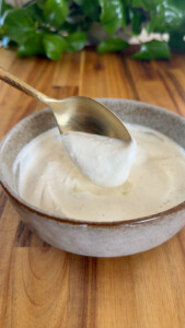 Spoon dipping into a bowl of yogurt sauce on a wooden table.