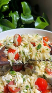 Close-up of orzo salad with cherry tomatoes, feta, and herbs in a wooden spoon.