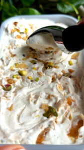 Scooping baklava ice cream topped with nuts in a container.