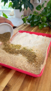 Mixing herbs and spices into flour and breadcrumbs on a tray.