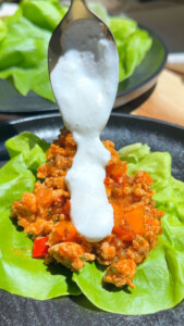 Lettuce wrap with minced meat filling topped with yogurt sauce being poured from a spoon.