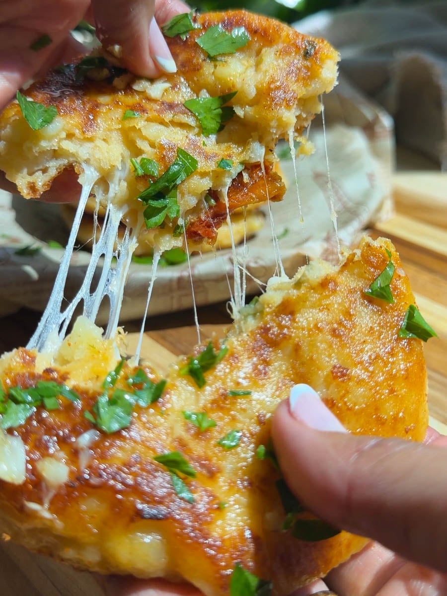 Cheesy stuffed tuna potato cakes are being pulled apart and sprinkled with fresh parsley.