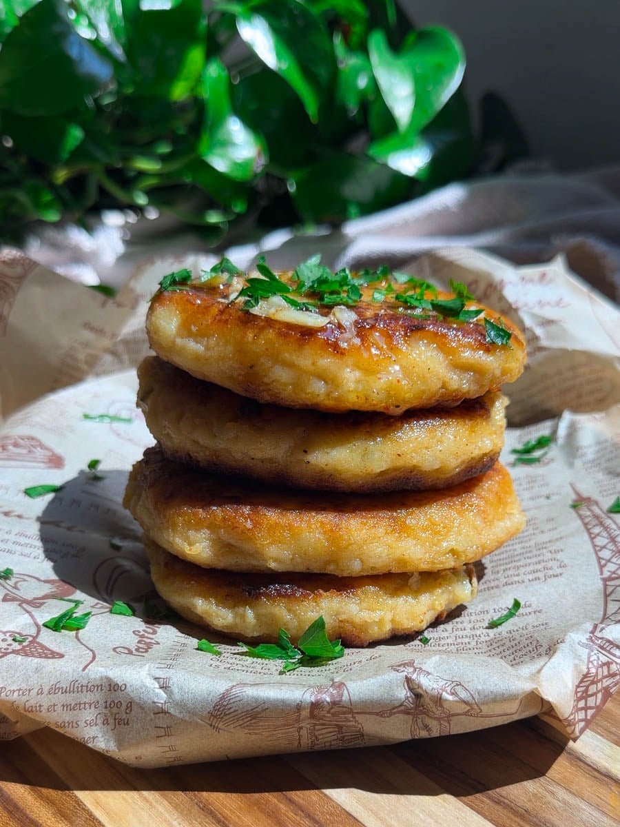 Stack of golden potato cakes garnished with fresh herbs on a parchment-lined wooden board.