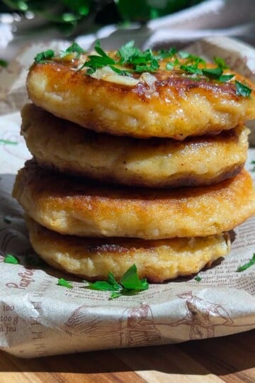 Stack of golden potato tuna cakes garnished with chopped parsley on parchment paper.