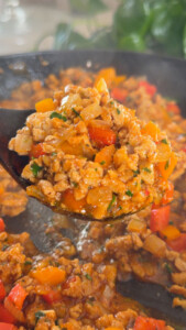 Sizzling ground meat with bell peppers in a skillet, garnished with herbs.