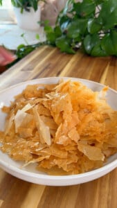 Crispy filo pastry flakes in white bowl on wooden table.