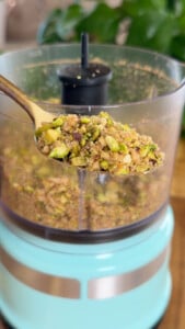 Chopped pistachios and walnuts in a food processor with spoon.