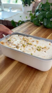 Pistachio and honey baklava ice cream in a white container on wooden countertop.