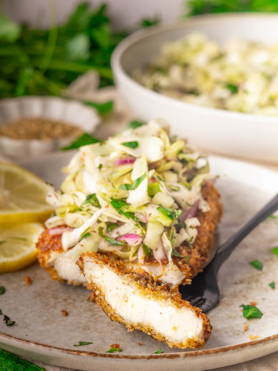 Za'atar chicken cutlet with Lebanese cabbage salad topped with fresh coleslaw on a plate with lemon slices.