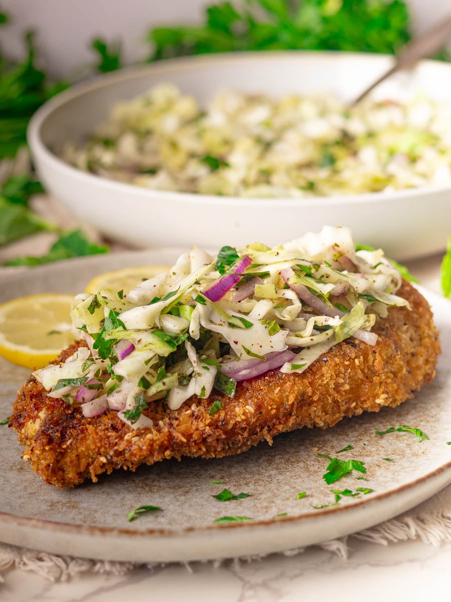 Za'atar chicken cutlet with Lebanese cabbage salad topped with fresh cabbage slaw on a rustic plate, garnished with lemon slices and parsley.